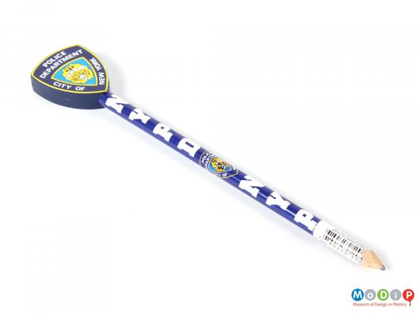 Top view of a New York Police Department pencil showing the blue and white shaft topped with a plastic representation of a police badge.