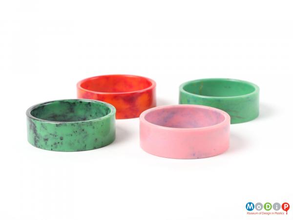 Side view of a set of four mottled napkin rings showing the pink and dark green rings at the front and the red and light green ring at the back.