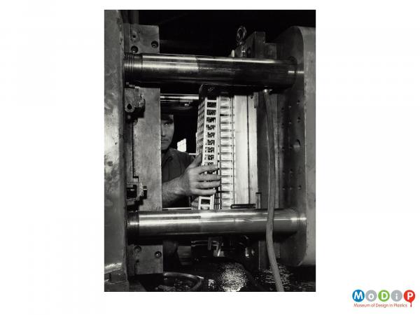 Scanned image showing a male worker removing an object from a mould.