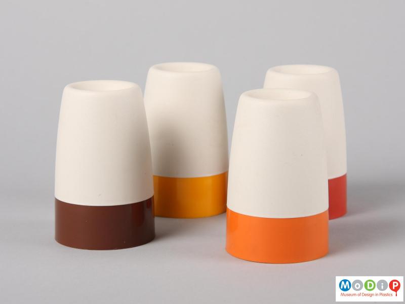 Side view of four Tupperware egg cups showing the plain sides of the cream cover and coloured bases of the cups.