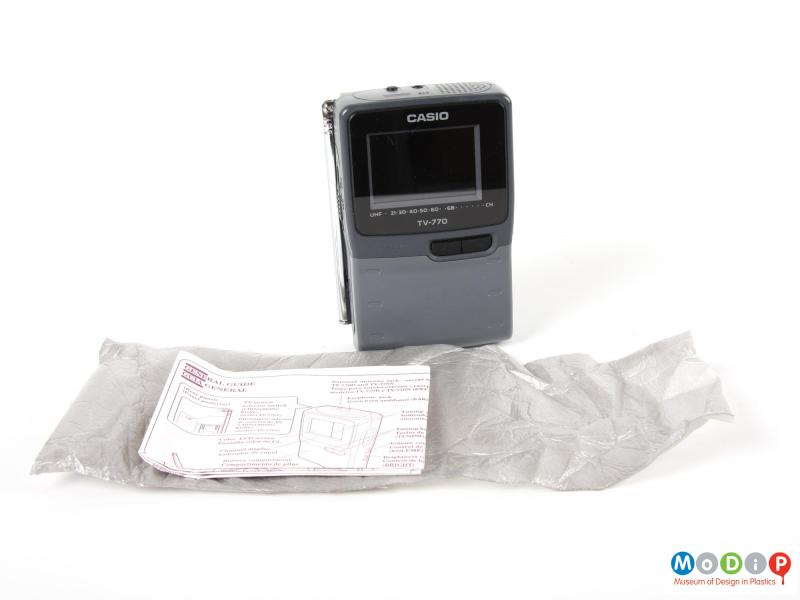 Front view of a Casio portable TV showing the instruction booklet and part of the packaging.