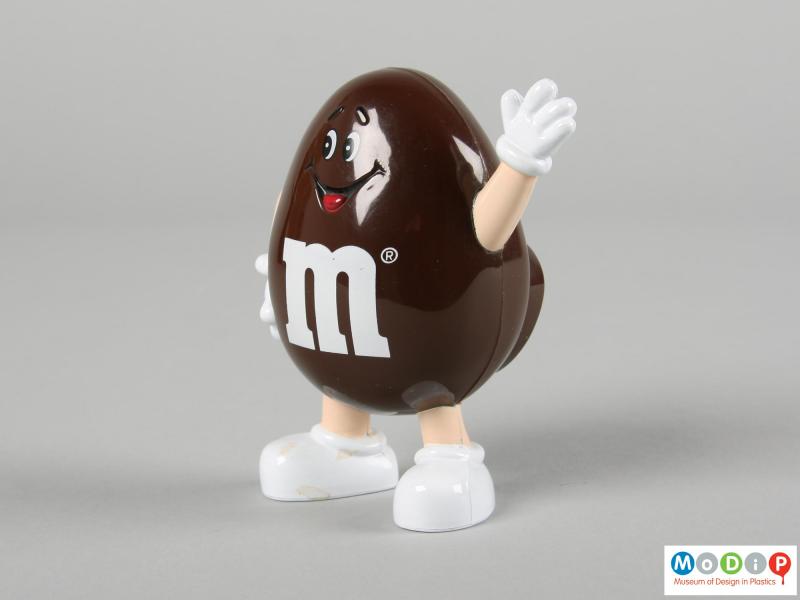 Side view of a brown M&M figure showing one hand in the air was if waving.