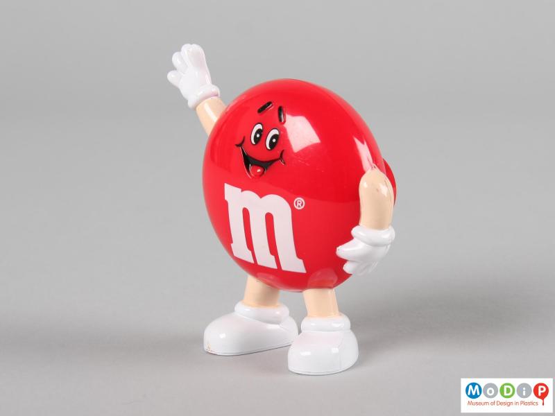 Side view of a brown M&M figure showing one arm held down by the side of the figure.