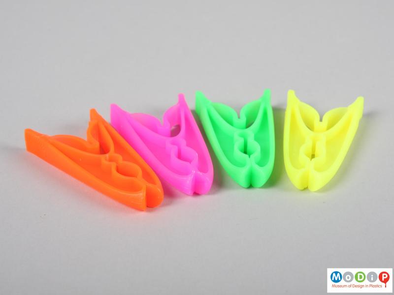 Side view of a packet of clothes pegs showing four pegs, one of each colour.