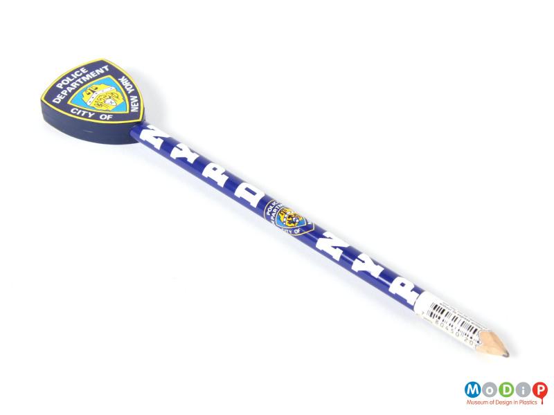 Top view of a New York Police Department pencil showing the blue and white shaft topped with a plastic representation of a police badge.