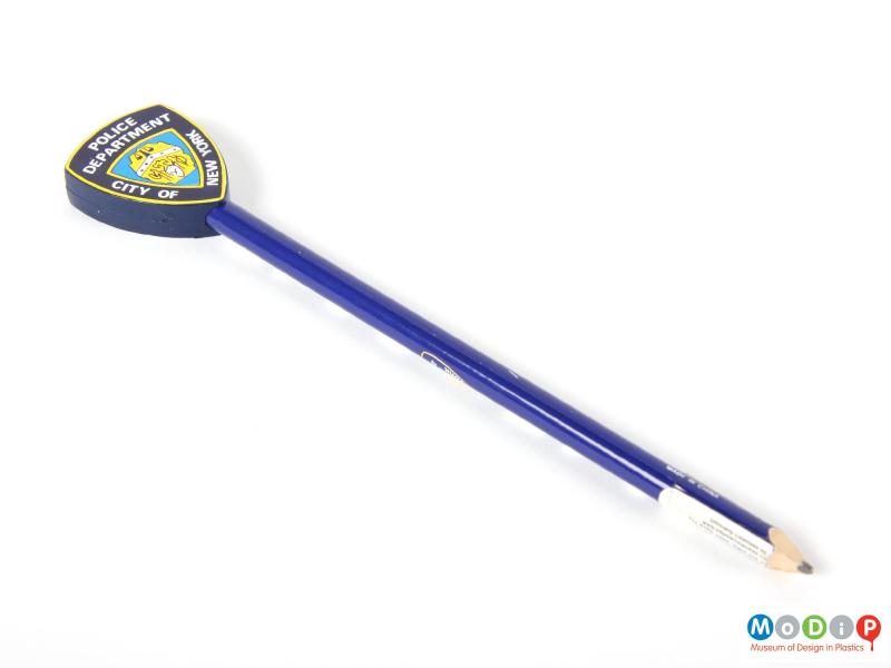 Underside view of a New York Police Department pencil showing the blue and white shaft topped with a plastic representation of a police badge.