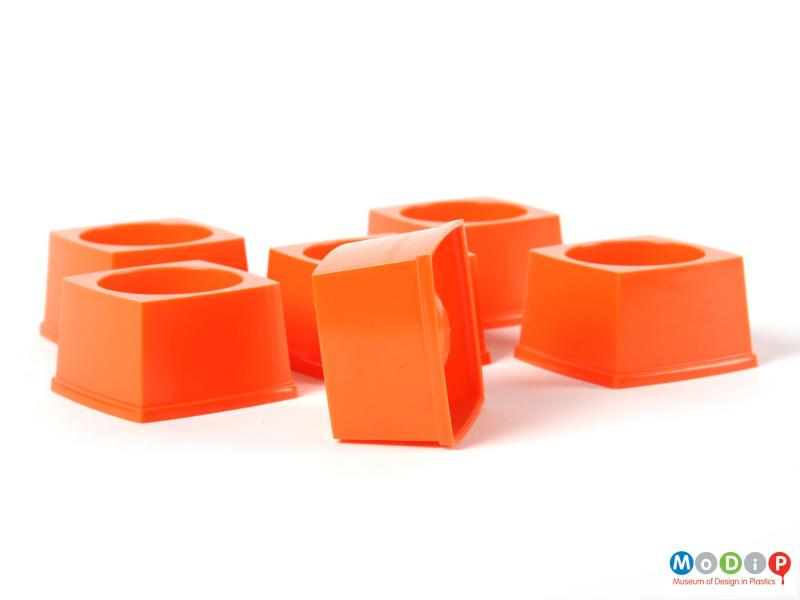 Side view of six stackable egg cups showing the sqaure shape and straight sides of the cups.  One cup is on its side exposing the underside of the cup including the injection moulding gate.