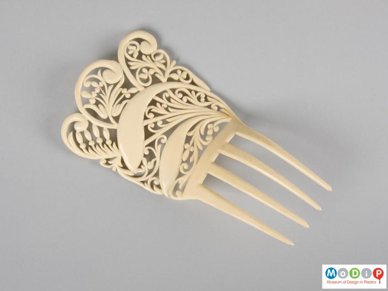 Top view of an imitation ivory comb showing the four teeth and the intricate design.