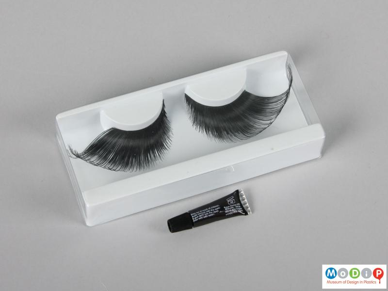 Top view of a pair of false eyelashes showing the tube of adhesive.