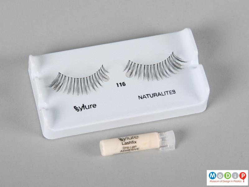 Top view of a pair of false eyelashes showing the tube of adhesive.