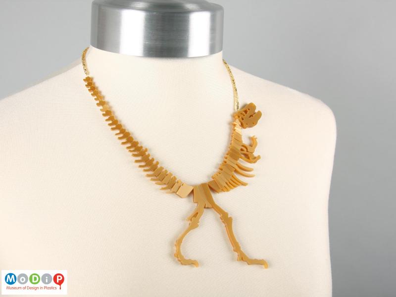 Front view of a Tatty Devine necklace showing the shape of the dinosaur on the neck of a mannequin.