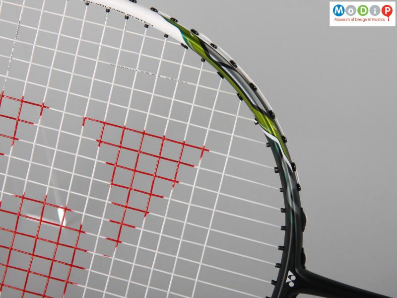 Close view of a badminton racket showing the junction between the frame and the strings.