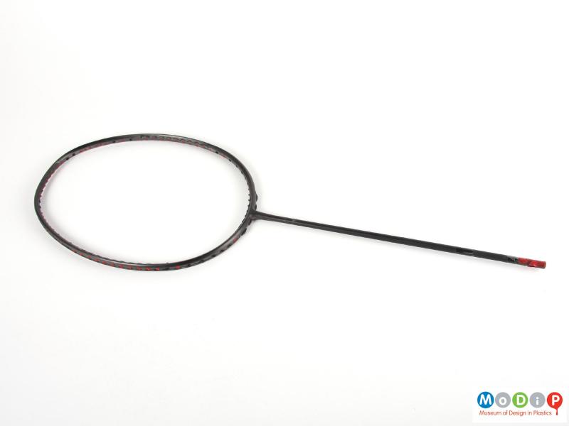 Side view of an unfinished badminton racket showing the straight handle and rounded head.