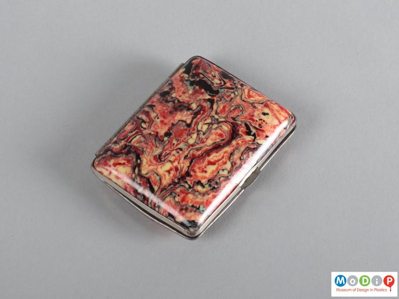 Top view of a cigaratte case showing the red, white, abd black marbled patterning.
