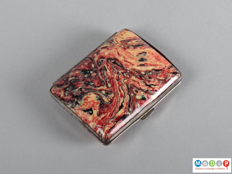 Underside view of a cigaratte case showing the red, white, abd black marbled patterning.
