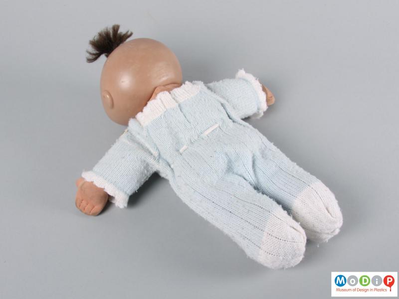 Rear view of a doll showing the top knot of hair and knitted clothing.