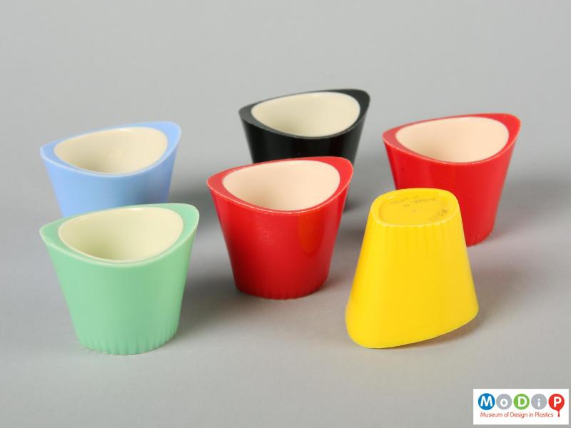 Side view of six Paramount egg cups showing the oval shape and the raised sides of the egg cup. One cup is sitting on its top to reveal the underside.