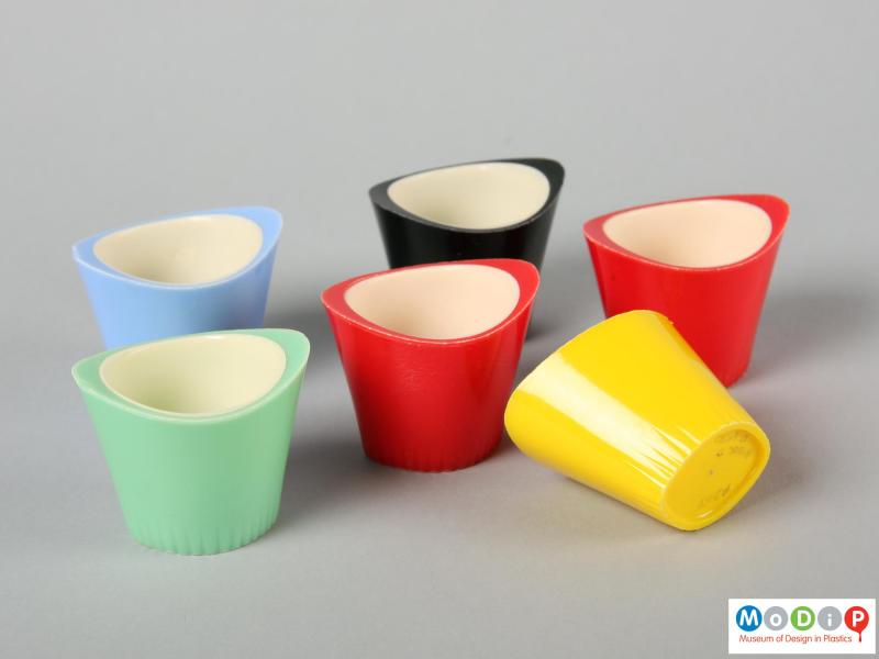Side view of six Paramount egg cups showing the oval shape and the raised sides of the egg cup. One cup is sitting on its side to reveal the small moulded foot running around the base edge of the cup.