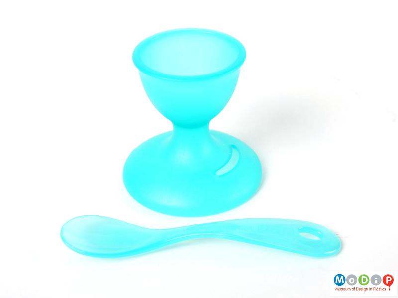 Side view of a Bodum egg cup with integral spoon showing the spoon out of the slot and laying in front of the egg cup.