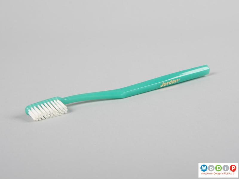 Side view of a toothbrush showing the thin handle and white bristles.