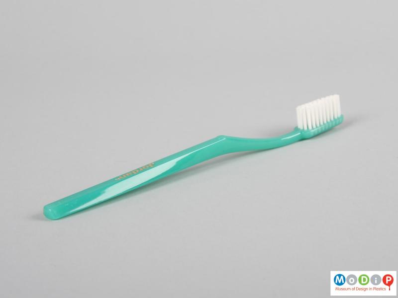 Side view of a toothbrush showing the thin handle and white bristles.