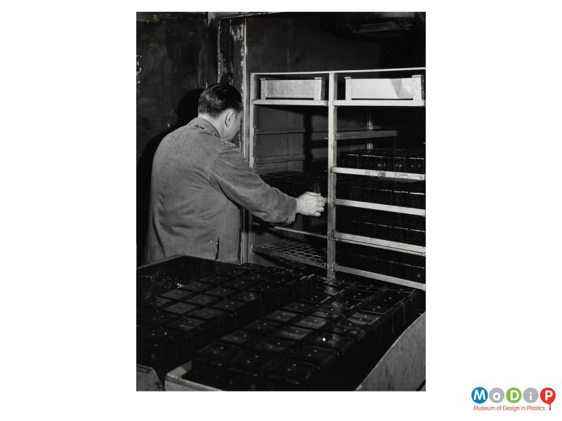 Scanned image showing a male worker moving trays of mouldings.