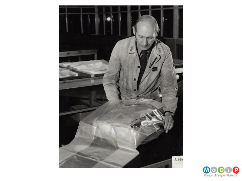 Scanned image showing a man putting a parcel into a polythene sack.
