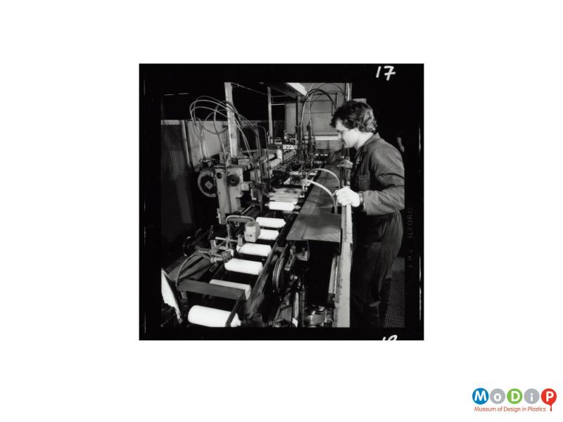 Scanned image showing a man at a bottle making machine.