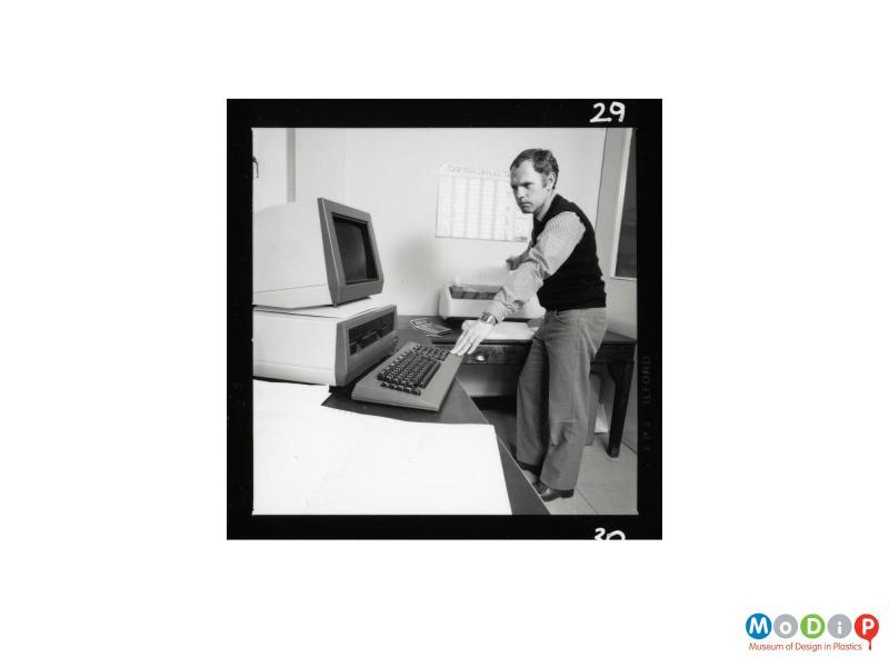 Scanned image showing a man standing at a computer and printer.