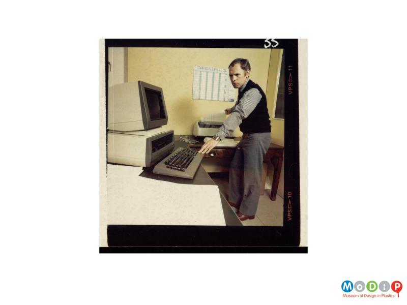 Scanned image showing a man standing at a computer and printer.
