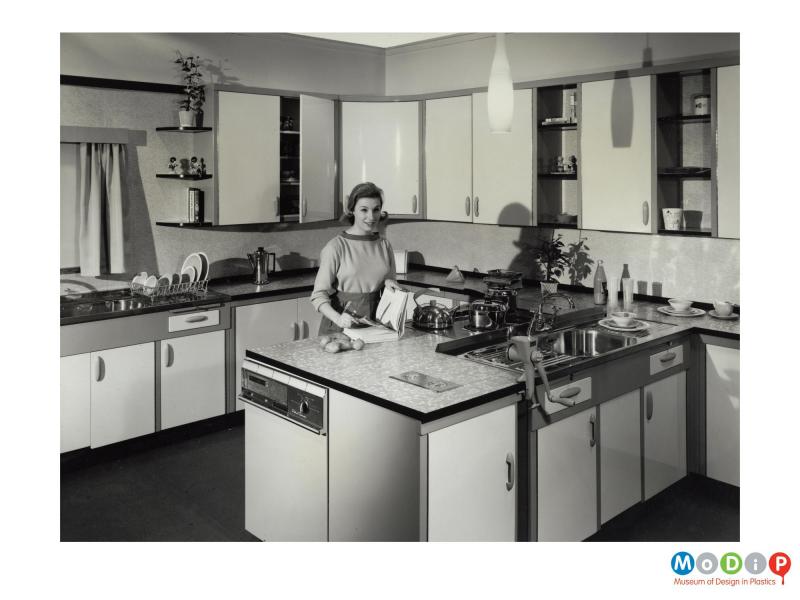 Scanned image showing female modelling a fitted kitchen.