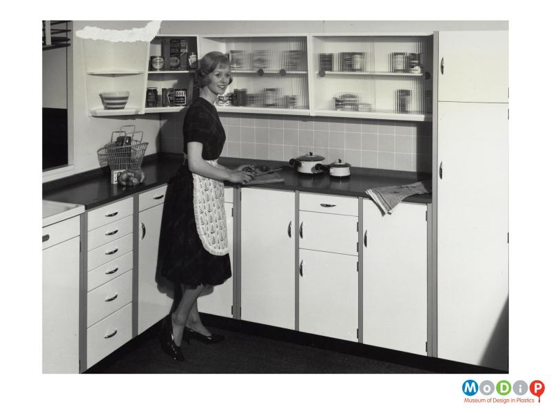 Scanned image showing a female modelling a fitted kitchen.