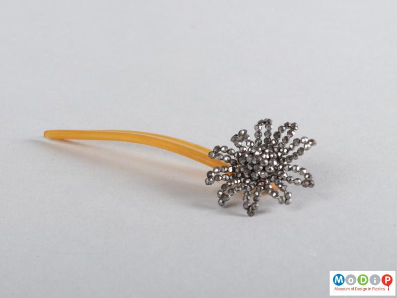 Side view of a hairpin showing the floral embellishment and two teeth.