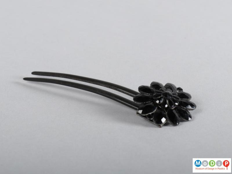 Side view of a hairpin showing the floral embellishment and two teeth.