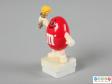 Side view of a red M&M figure showing one hand the torch aloft the other held down low.