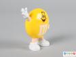 Side view of a yellow M&M figure showing on hand raised in the air as if waving.
