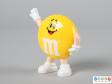 Side view of a yellow M&M figure showing one hand down by the figure's side.