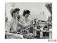Scanned image showing two women removing filled tubes from a sealing machine.