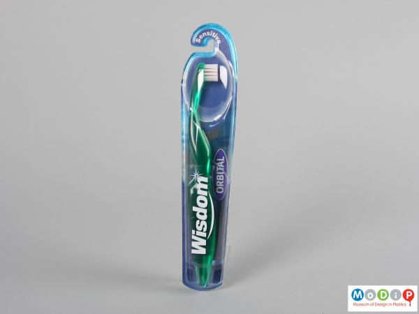 Front view of a packaged toothbrush showing the ergonomic shape of the handle and the round head.
