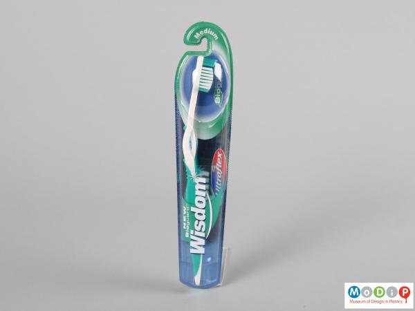 Front view of a packaged toothbrush showing the flexible design in the neck of the handle.
