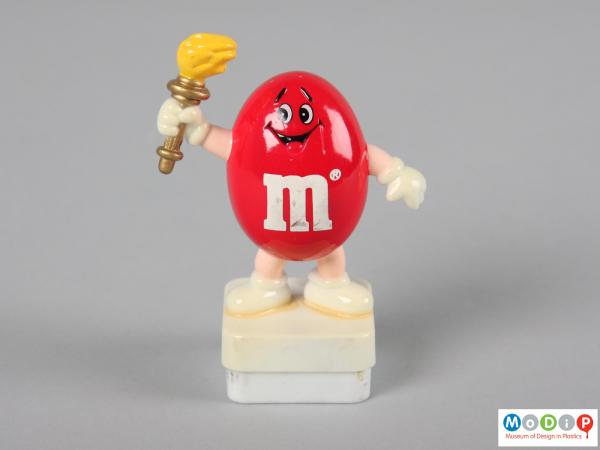 Front view of a red M&M figure showing the smiling face and the limbs.