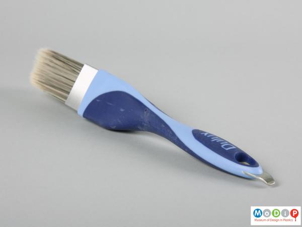 Side view of a paint brush showing the metal hook on the end of the handle used to open paint cans.