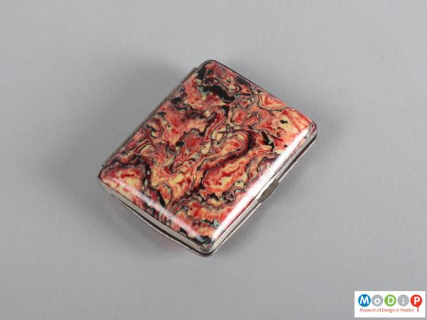 Top view of a cigaratte case showing the red, white, abd black marbled patterning.
