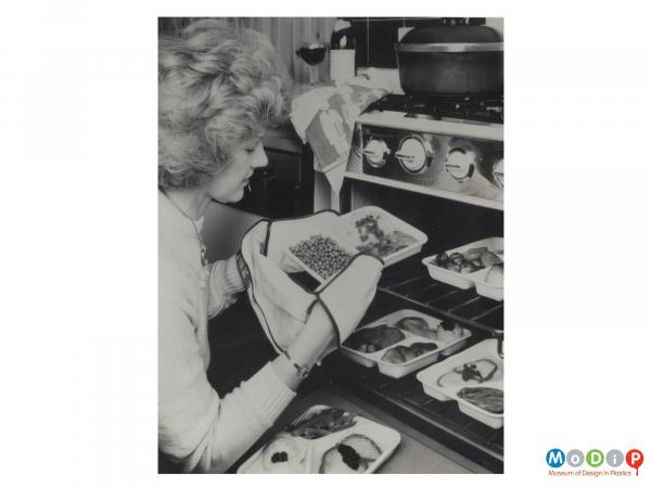 Scanned image showing a lady putting ready meals into an oven.