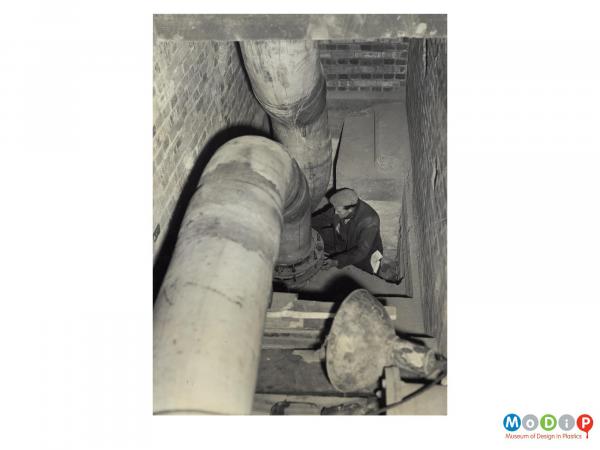 Scanned image showing a man joining a ceramic and plastic pipe.