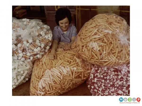 Scanned image showing a female worker surrounded by large bags of tubes.