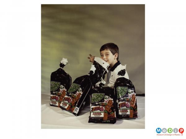 Scanned image showing a young boy with bags of crisps.