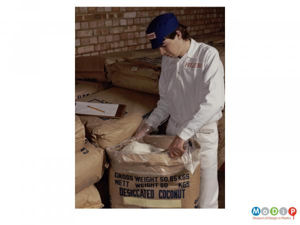 Scanned image showing a man scooping dessicated coconut from a sack.