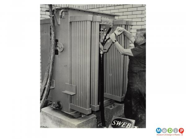 Scanned image showing a man maintaining cables in a large junction box.