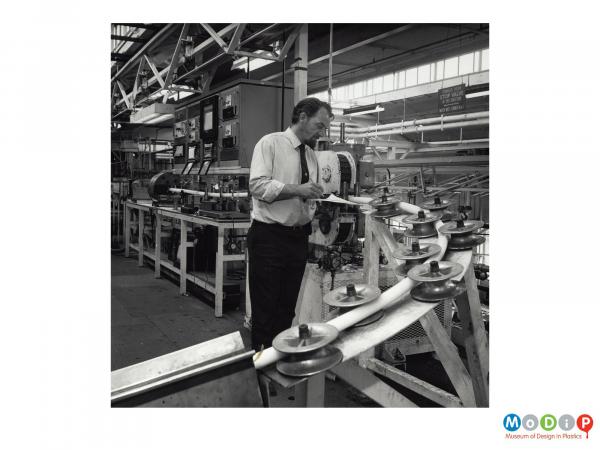 Scanned image showing a male employee inspecting the production of cable.